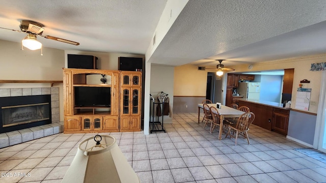 tiled living room featuring ceiling fan, a fireplace, and a textured ceiling