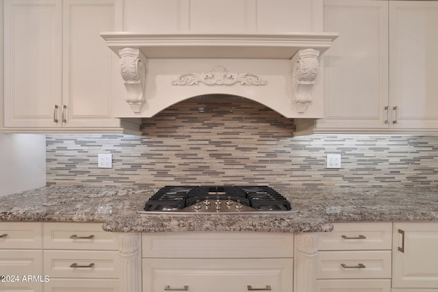 kitchen featuring light stone counters, white cabinets, backsplash, and stainless steel gas cooktop