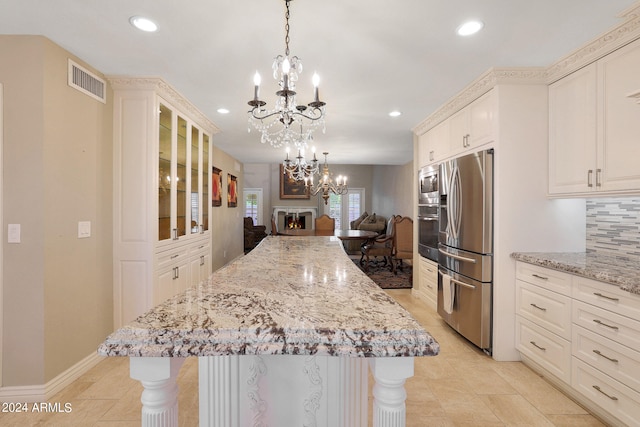 kitchen featuring light stone counters, pendant lighting, a kitchen island, backsplash, and appliances with stainless steel finishes