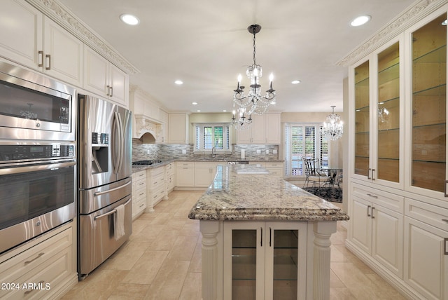 kitchen featuring a kitchen island, hanging light fixtures, light stone countertops, backsplash, and appliances with stainless steel finishes