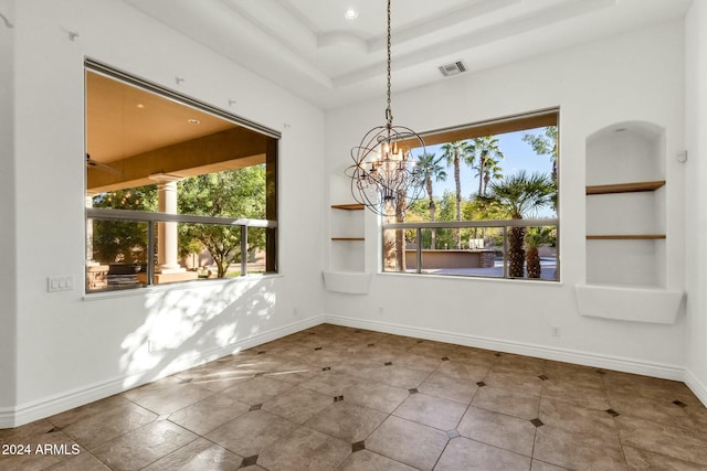 unfurnished dining area featuring a tray ceiling, built in shelves, and a notable chandelier