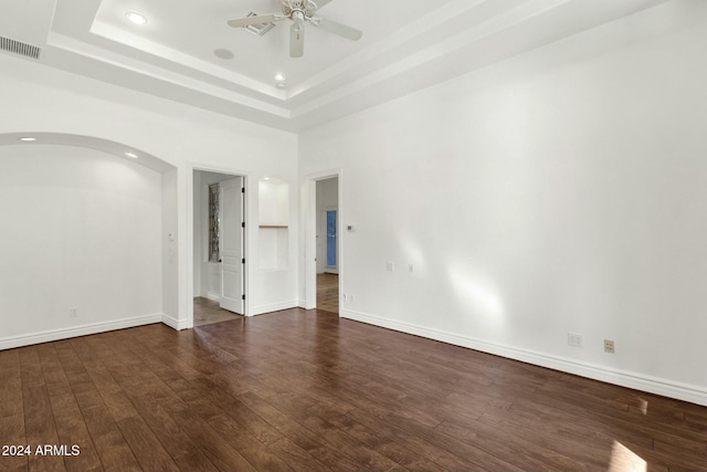 unfurnished room with ceiling fan, a raised ceiling, and dark wood-type flooring