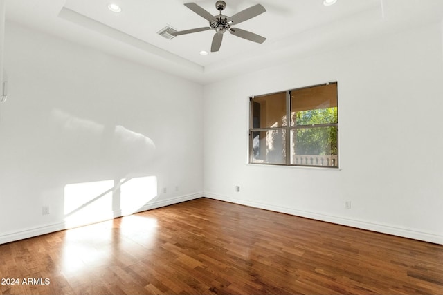 spare room with wood-type flooring, a tray ceiling, and ceiling fan