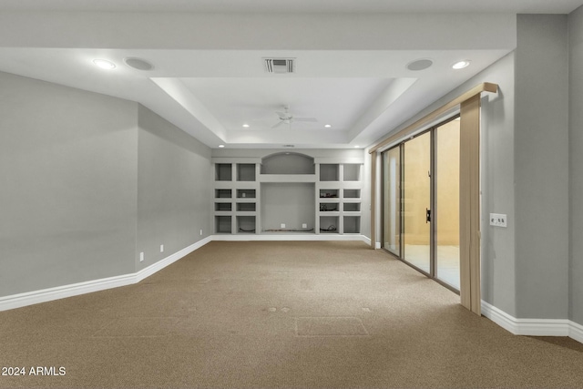 unfurnished living room featuring a raised ceiling, ceiling fan, built in features, and carpet floors