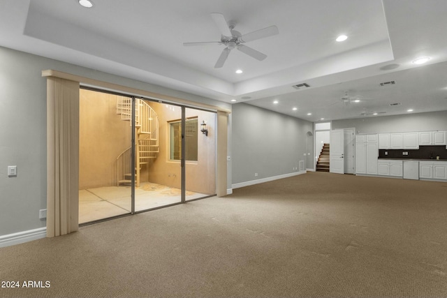 unfurnished living room featuring light colored carpet, ceiling fan, and a tray ceiling