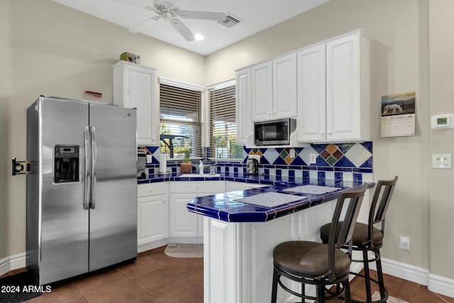 kitchen featuring kitchen peninsula, appliances with stainless steel finishes, decorative backsplash, white cabinets, and tile counters