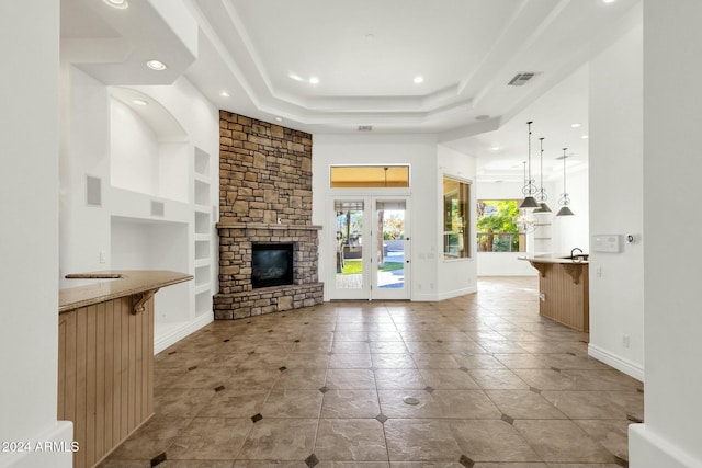 unfurnished living room featuring built in shelves, a raised ceiling, a fireplace, and french doors