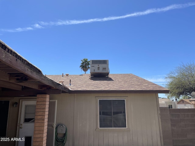 view of property exterior with roof with shingles, fence, and central AC unit