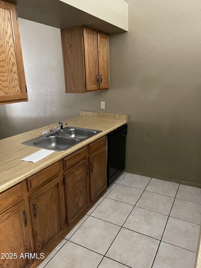 kitchen with black dishwasher, light countertops, light tile patterned floors, and a sink