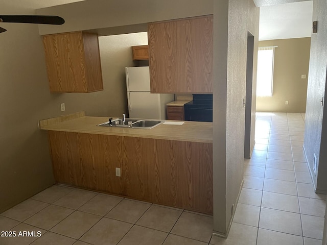 kitchen with freestanding refrigerator, a sink, a peninsula, and light tile patterned floors