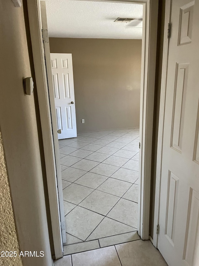 corridor with visible vents, a textured ceiling, and light tile patterned flooring