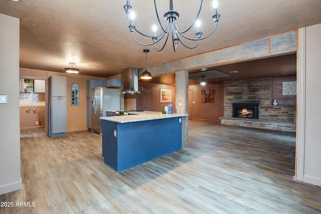 kitchen featuring ventilation hood, light hardwood / wood-style floors, a fireplace, stainless steel fridge with ice dispenser, and decorative light fixtures