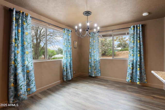 unfurnished dining area featuring hardwood / wood-style flooring, an inviting chandelier, and a textured ceiling