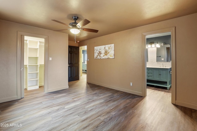 unfurnished bedroom with ensuite bathroom, a spacious closet, light hardwood / wood-style flooring, a closet, and ceiling fan