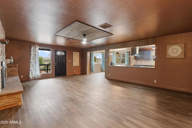 unfurnished living room with a stone fireplace, a textured ceiling, ceiling fan, and hardwood / wood-style flooring