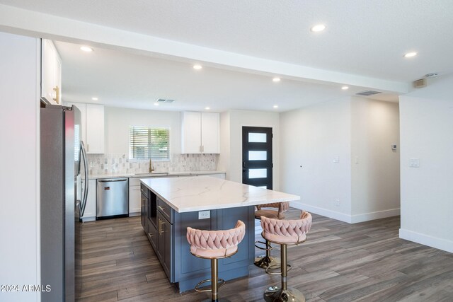 kitchen with appliances with stainless steel finishes, tasteful backsplash, white cabinetry, sink, and a kitchen island