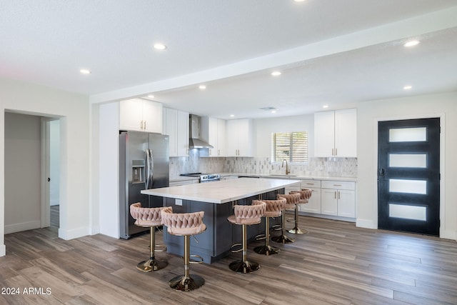 kitchen with appliances with stainless steel finishes, white cabinetry, a kitchen island, a breakfast bar, and wall chimney exhaust hood