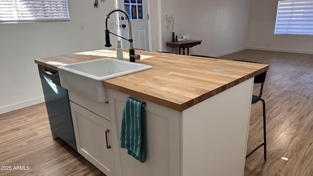 kitchen featuring a breakfast bar, sink, a center island with sink, dishwasher, and white cabinetry