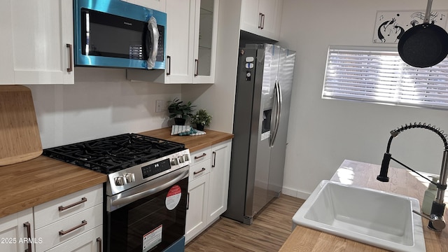 kitchen featuring sink, stainless steel appliances, butcher block countertops, light hardwood / wood-style floors, and white cabinets