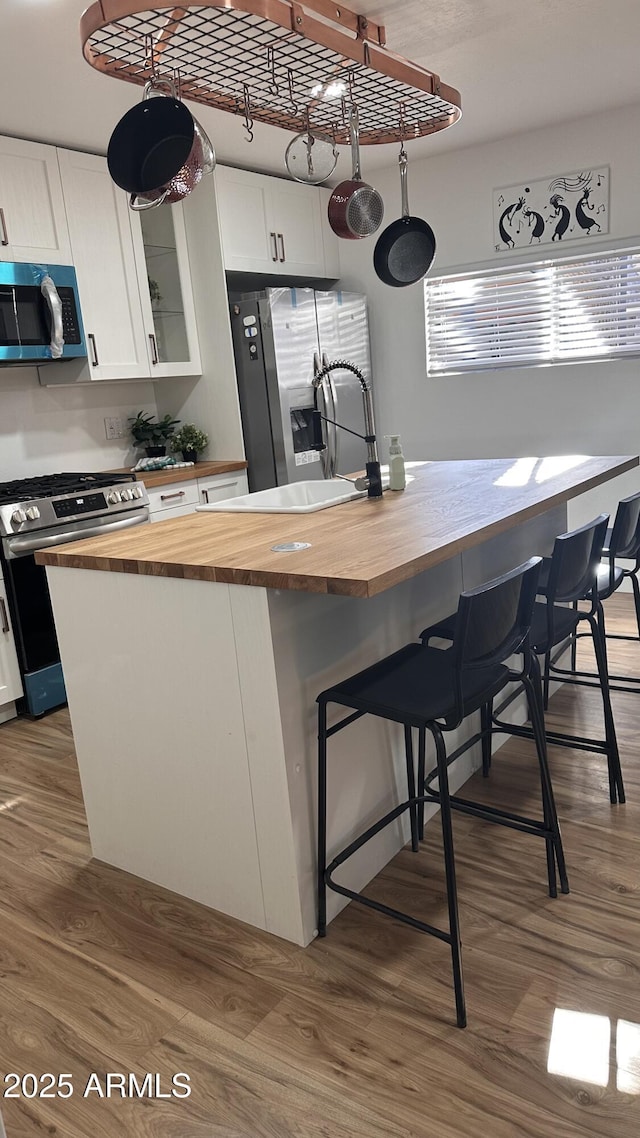 kitchen with wooden counters, a kitchen bar, stainless steel appliances, and white cabinetry