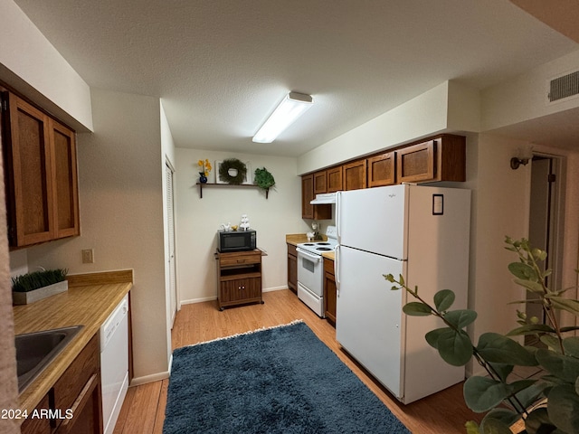 kitchen with a textured ceiling, sink, light hardwood / wood-style floors, and white appliances