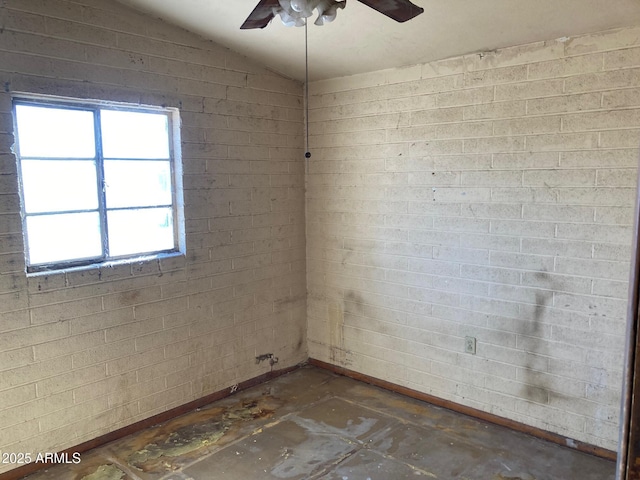 unfurnished room with lofted ceiling, ceiling fan, and brick wall