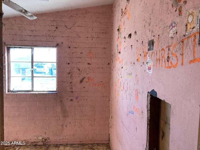 spare room featuring brick wall and lofted ceiling