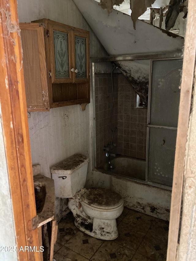 bathroom featuring tile patterned flooring, combined bath / shower with glass door, and toilet