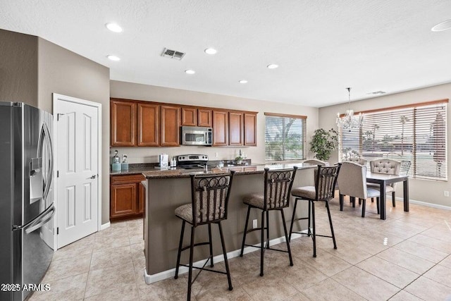 kitchen featuring a kitchen bar, dark stone counters, hanging light fixtures, stainless steel appliances, and a center island with sink