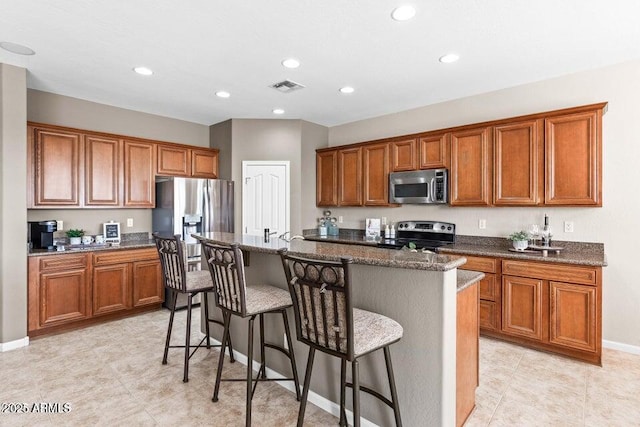 kitchen with dark stone countertops, a kitchen bar, an island with sink, and appliances with stainless steel finishes