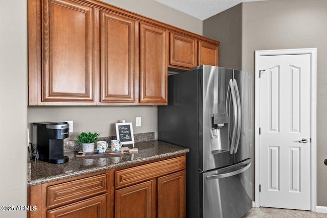 kitchen featuring stainless steel refrigerator with ice dispenser and dark stone counters