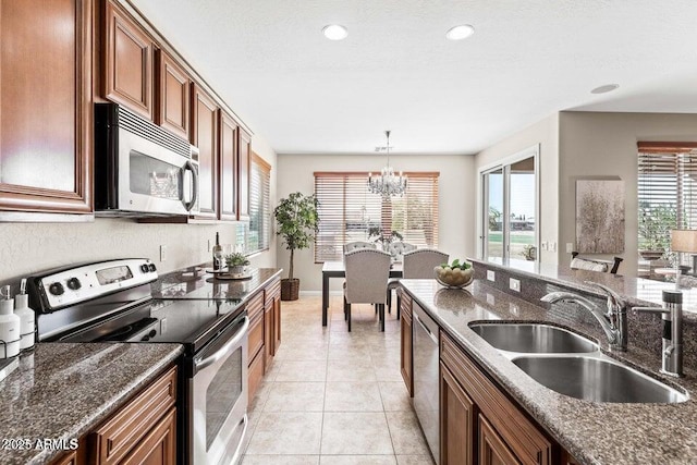 kitchen with sink, hanging light fixtures, light tile patterned floors, appliances with stainless steel finishes, and dark stone counters