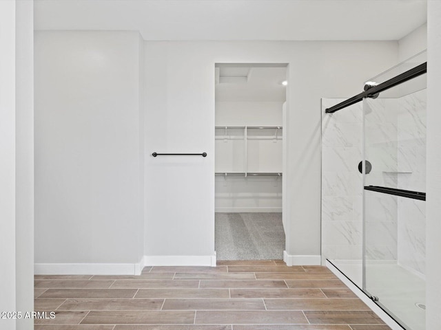 bathroom with wood tiled floor, a walk in closet, baseboards, and a marble finish shower