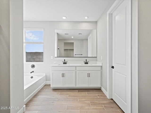 bathroom with double vanity, wood finish floors, a sink, and a bath