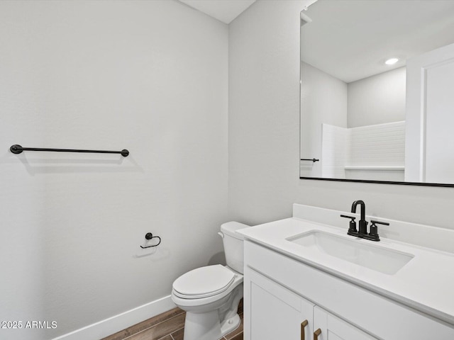 bathroom featuring toilet, baseboards, wood finished floors, and vanity