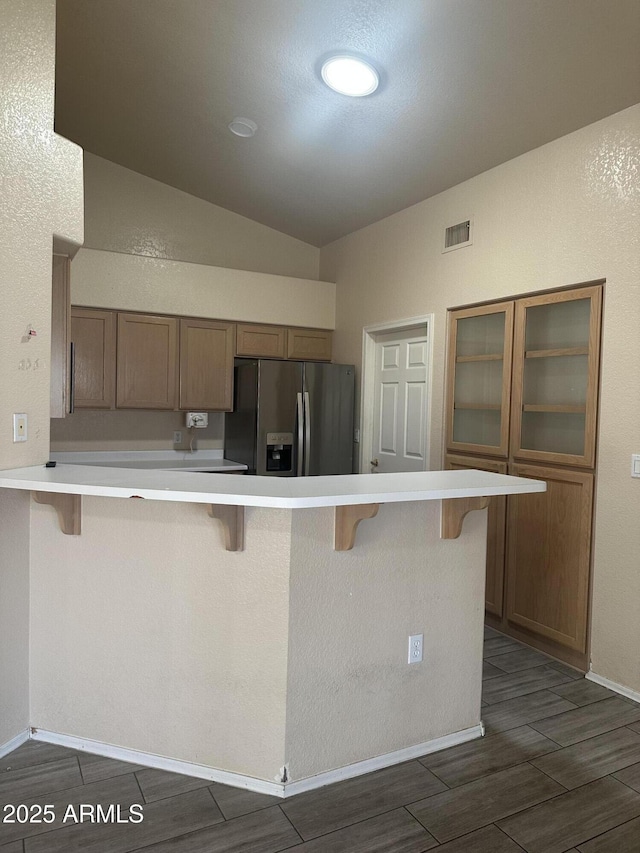 kitchen featuring visible vents, vaulted ceiling, a kitchen breakfast bar, a peninsula, and stainless steel refrigerator with ice dispenser