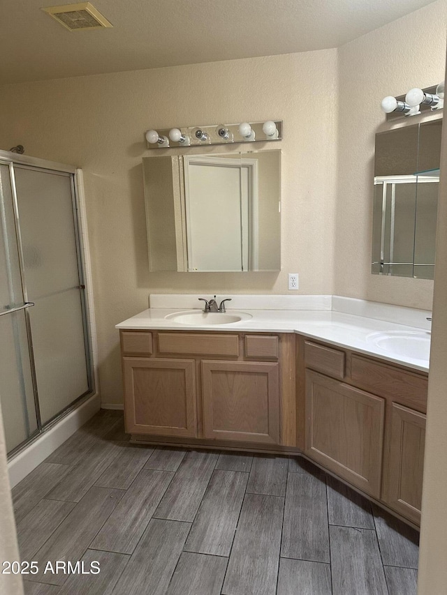 bathroom featuring double vanity, a stall shower, visible vents, and a sink