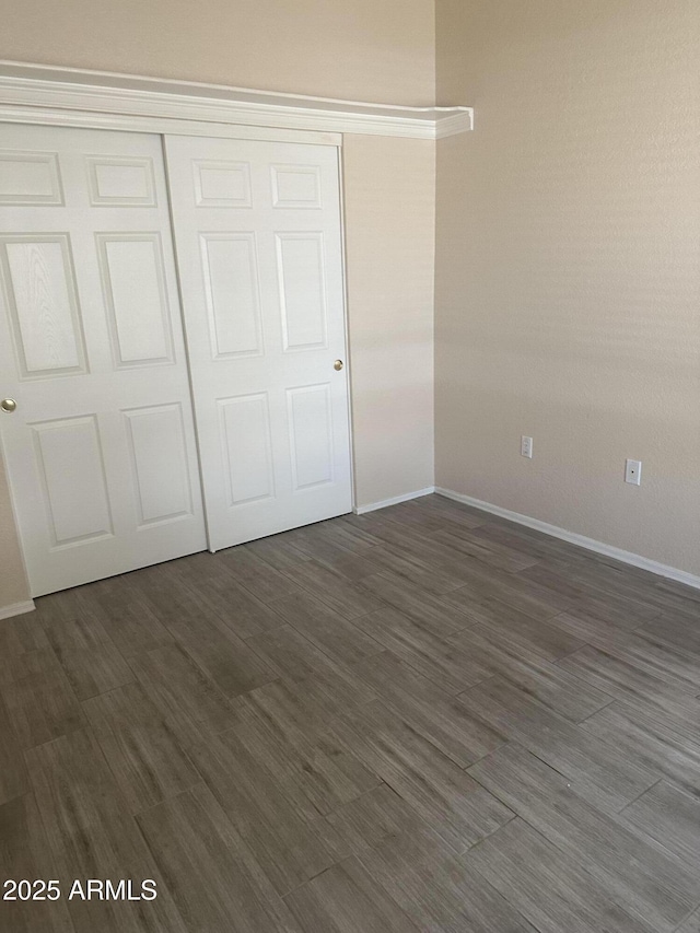 unfurnished bedroom with a closet, baseboards, and dark wood-style flooring