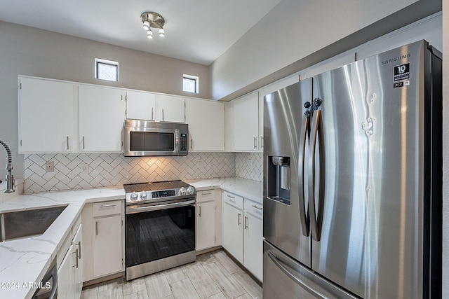 kitchen featuring appliances with stainless steel finishes, light stone countertops, decorative backsplash, sink, and white cabinets