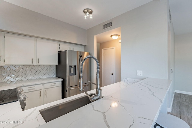 kitchen featuring white cabinetry, light stone countertops, wood-type flooring, stainless steel fridge with ice dispenser, and decorative backsplash