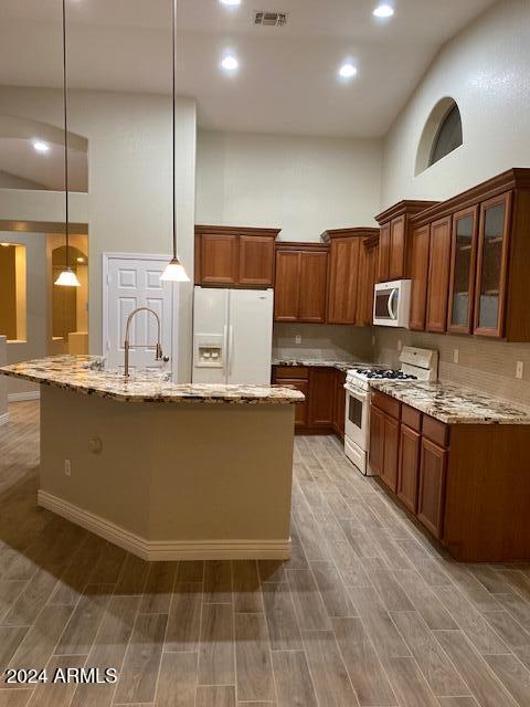 kitchen featuring white appliances, a high ceiling, light stone countertops, light wood-type flooring, and decorative light fixtures