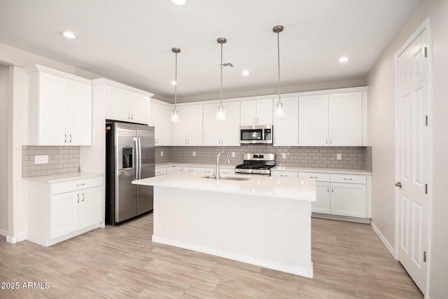 kitchen with sink, hanging light fixtures, a kitchen island with sink, white cabinets, and appliances with stainless steel finishes