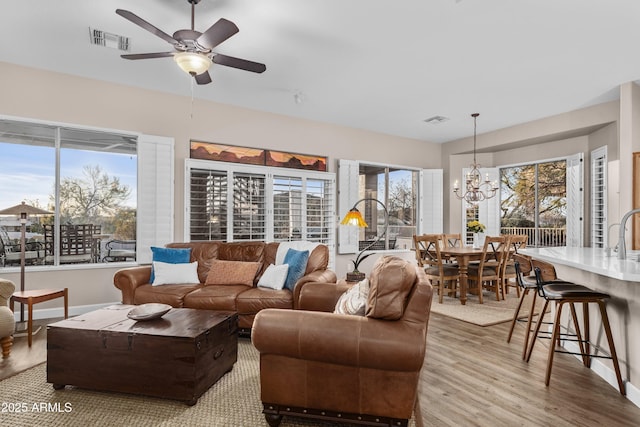 living room with ceiling fan with notable chandelier and light hardwood / wood-style flooring