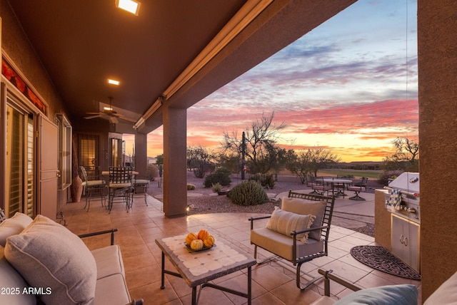 patio terrace at dusk featuring exterior kitchen, an outdoor hangout area, ceiling fan, and grilling area