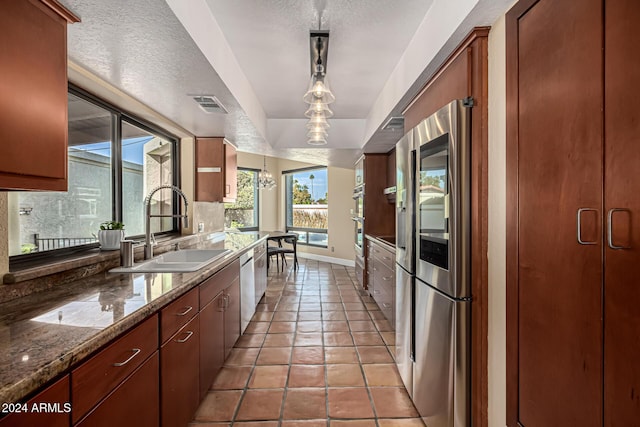 kitchen featuring a textured ceiling, stainless steel appliances, sink, decorative light fixtures, and dark stone countertops