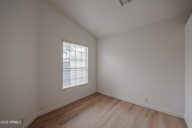 spare room with lofted ceiling, light wood finished floors, visible vents, and baseboards