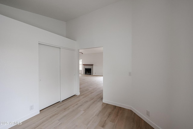 unfurnished room featuring light wood-type flooring, a high ceiling, a fireplace, and baseboards