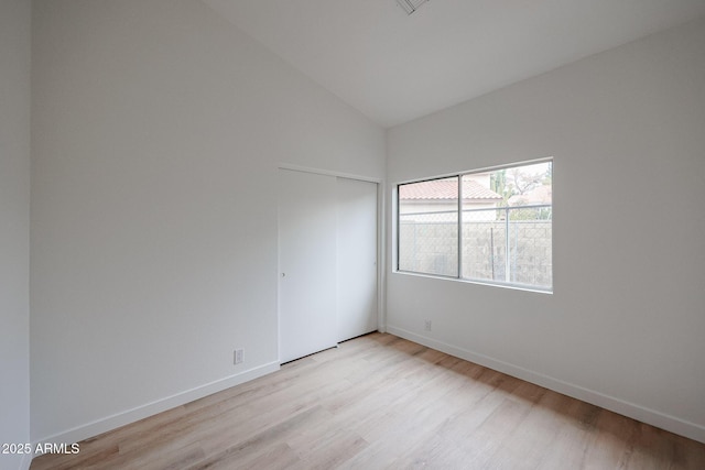 empty room with vaulted ceiling, light wood-type flooring, and baseboards