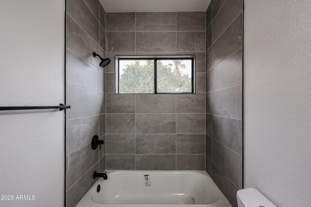 bathroom with toilet, a textured wall, and bathing tub / shower combination