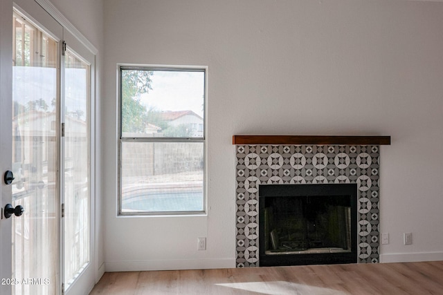 unfurnished living room featuring a tiled fireplace, wood finished floors, and baseboards